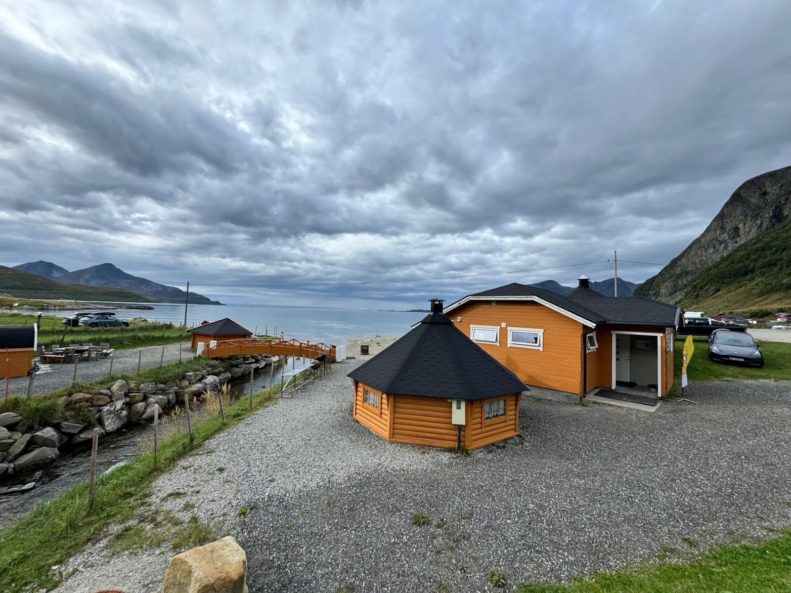 Kaféens oransje trebygning nede ved sjøen i Grøtfjord med fjell i bakgrunnen