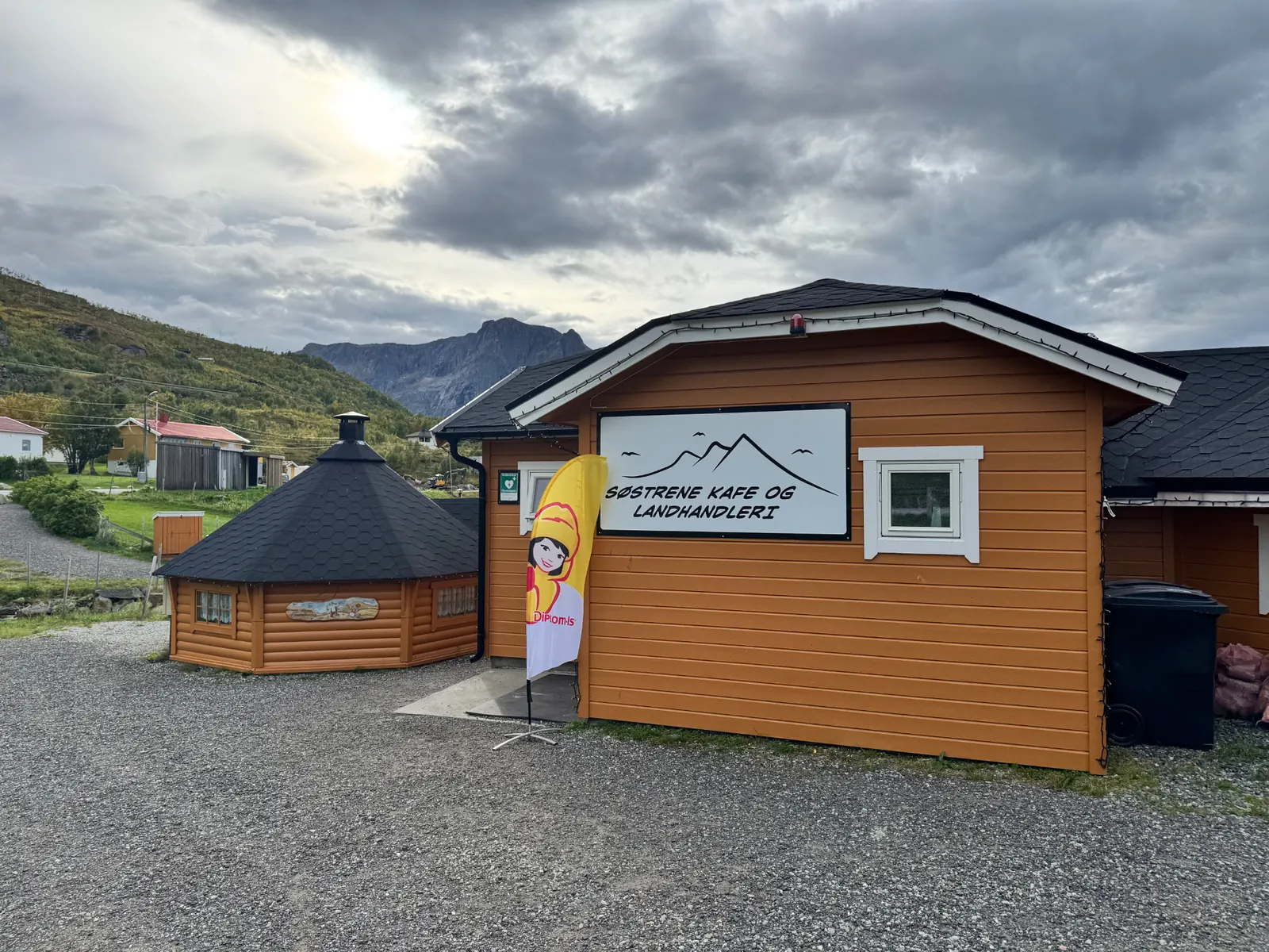 Skilt på kaféens oransje trebygning med teksten Søstrene Kafe og Landhandleri