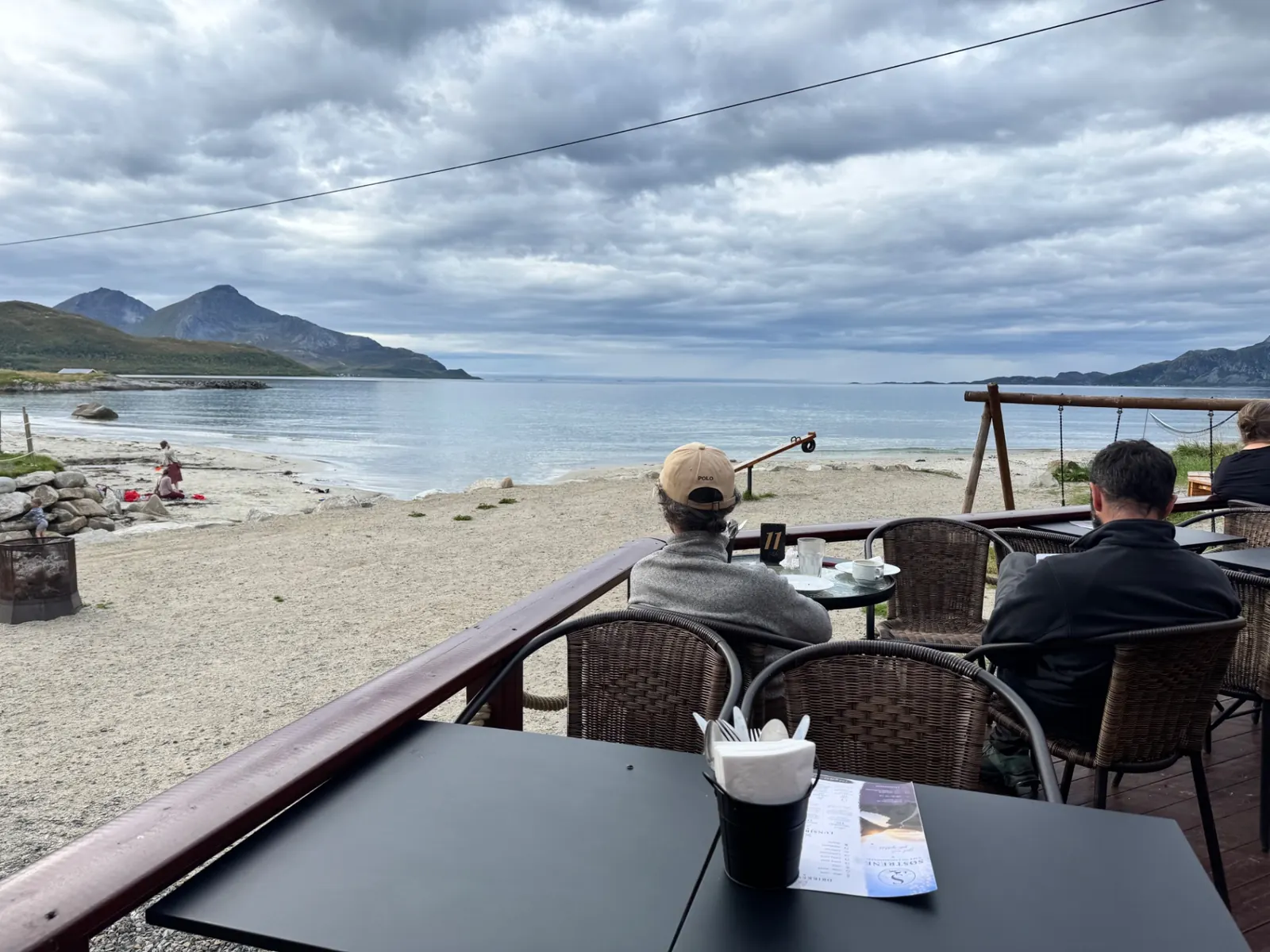 Uteservering med bord og stoler med utsikt over sandstranda i Grøtfjord